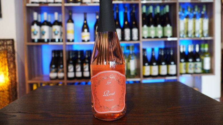 Café Leopold Schwechat, © Café Leopold A bottle of rosé wine stands on a table in front of a wine rack.
