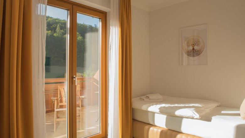 Single room with balcony, © Dorfschmiede eG Single room with balcony, bed, yellow curtains, wooden balcony, sunny.