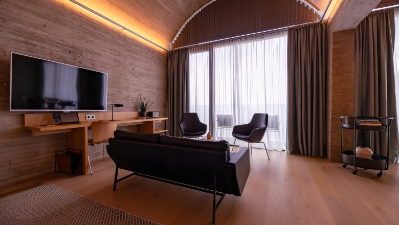 LOISIUM Langenlois, © Niederösterreich Werbung / Maximilian Pawlikowsky Modern living room with wooden ceiling, sofa, armchair and large window.