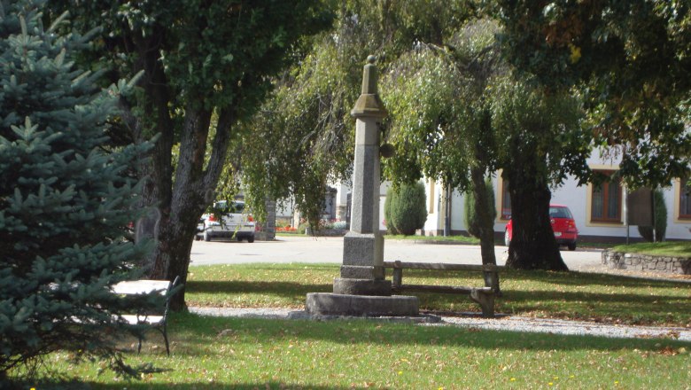 Market town of Grafenschlag, © Marktgemeinde Grafenschlag A small park with a stone monument and a bench surrounded by trees.
