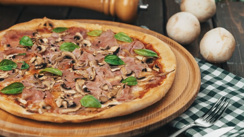 Fresh products are processed, © cervodoro Pizza with ham, mushrooms and basil on a wooden board.