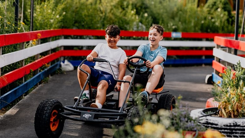 Kittenberg adventure gardens, © Matthias Streibel Two boys drive laughing in a go-kart on a track with red and white fences.