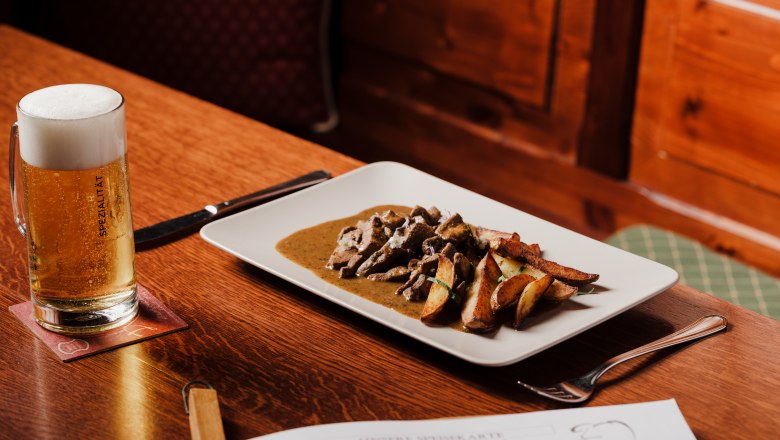 Forgotten dishes are also served here, © Niederösterreich Werbung/Michael Reidinger Table with beer and plate with meat dish in a rustic ambience.