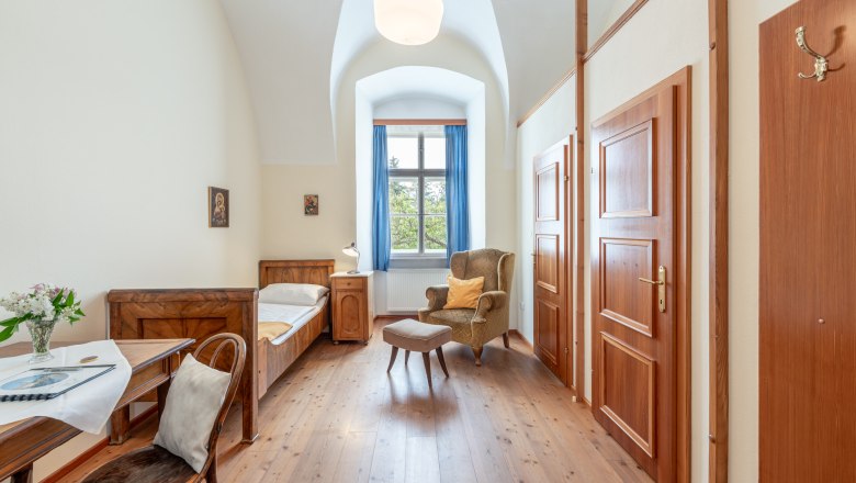 StiftAltenburg_single room, © Martin Mathes Single room in Altenburg Abbey with bed, armchair, table and window with blue curtains.