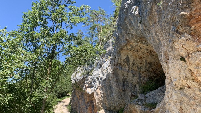 Falkenstein Nature Park, © Tourismusverband Semmering-Rax-Schneeberg A hiking trail in the Falkenstein Nature Park leads past a rock face with a cave, surrounded by trees and blue sky.