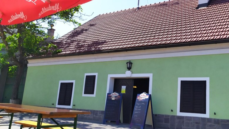 Wine tavern Maier exterior view, © Weinbau Maier Exterior view of a traditional wine tavern with green paint and red roof tiles. There are wooden benches and a red parasol in front of the building.
