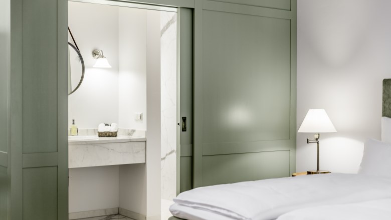 Hotel zum Glockenturm, © croce&wir Hotel room with green sliding-door wardrobe, bed and view of the bathroom.