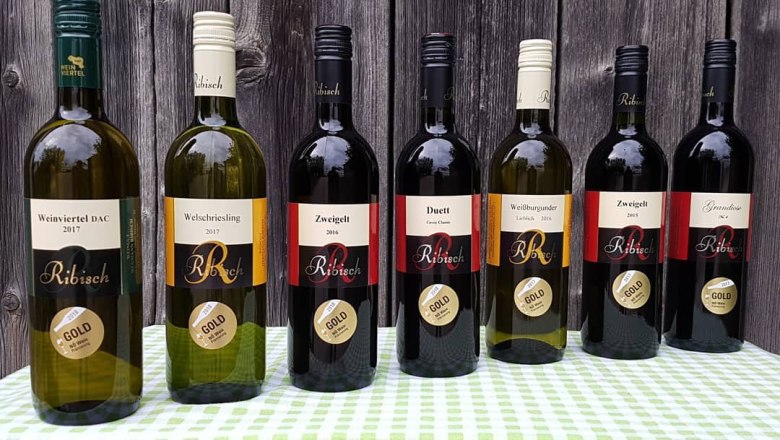 Wine assortment, © Weingut Ribisch Seven bottles of Ribisch wine on a table in front of a wooden wall.