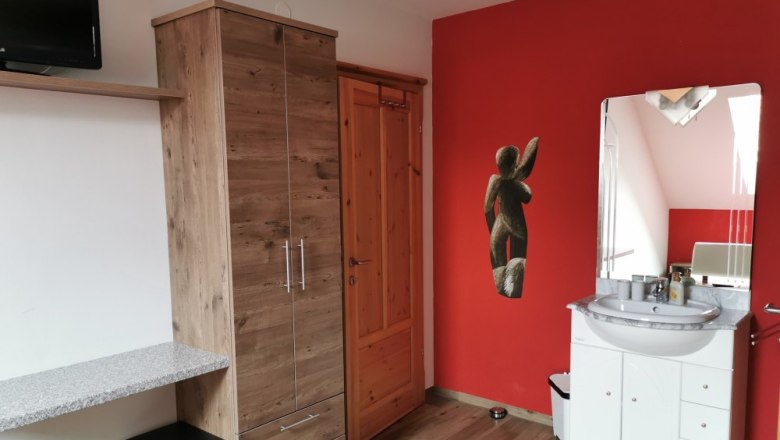 Room "Fanny", © Weinhof Brauner Room with red wall, wooden cupboard, washbasin and mirror.