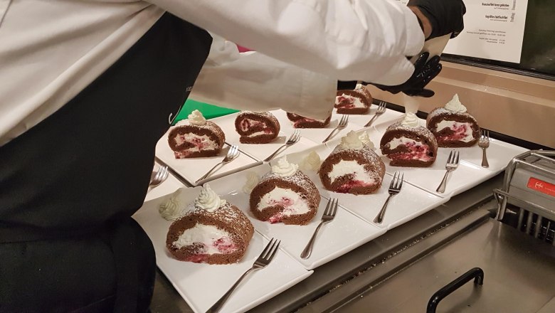 Desserts, © Reef & Beef A chef decorates chocolate sponge rolls with cream on white plates.