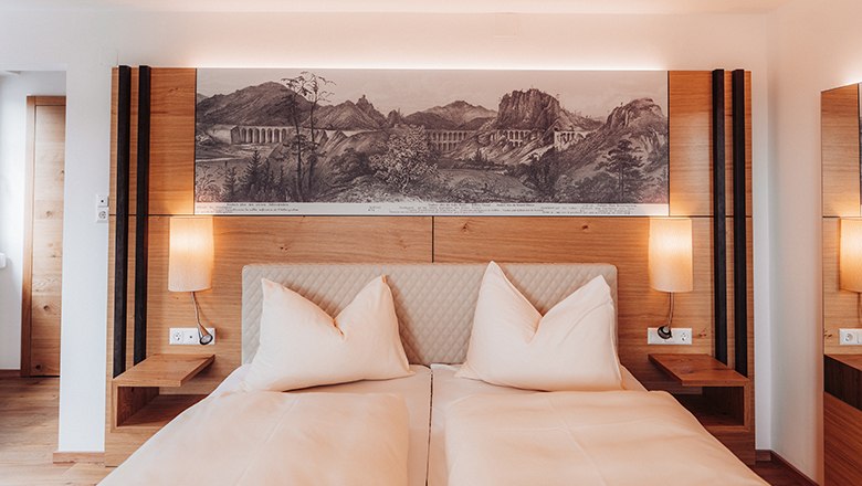 Premium double room with balcony, © Payerbacherhof - Christopher Tarkus A modern double room with two beds, wooden furniture and a landscape painting above the bed.