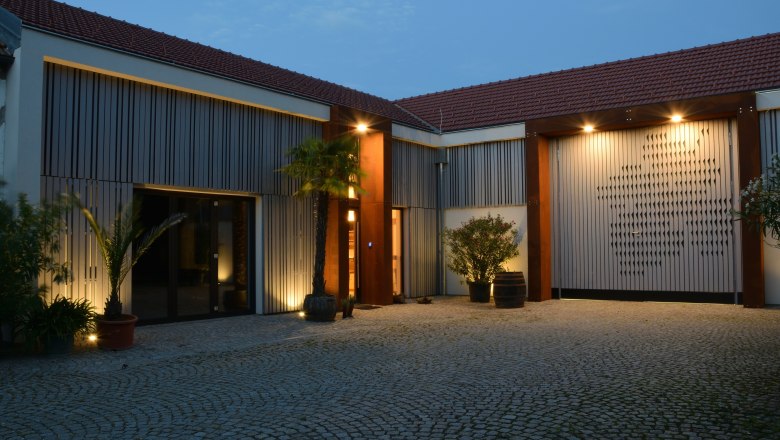 Winery, © Sophie Kienberger Illuminated courtyard of a modern winery with palm trees and cobblestones.