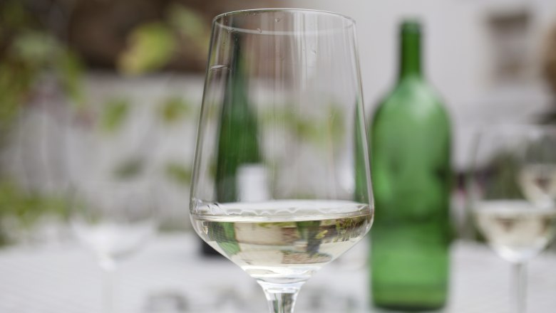 Wine glass, © Weinviertel Tourismus / Christine Wurnig A wine glass with white wine on a table, a green wine bottle in the background.
