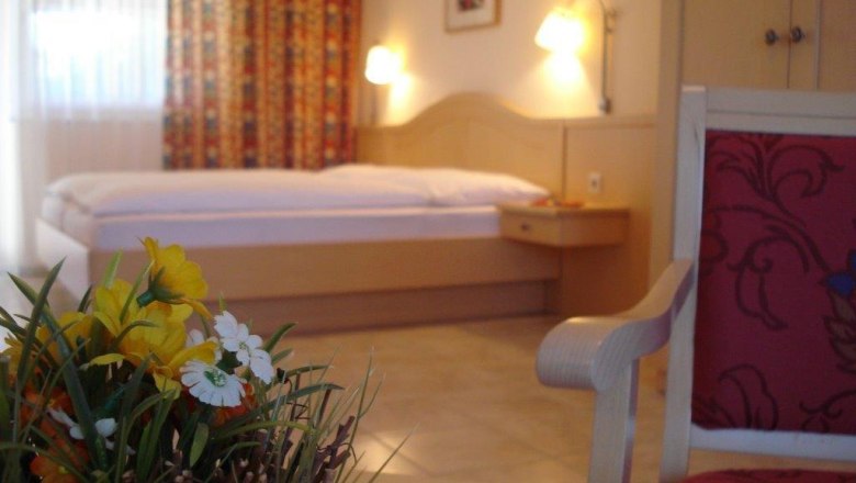 Guest room, © Pension Rudi A cozy guest room with a bed, a chair and a table with flowers.
