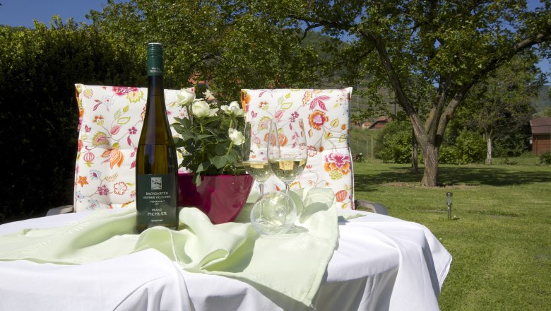 Garden, © www.wachaufoto.at A table in the garden with a bottle of wine, two glasses and a bouquet of flowers.