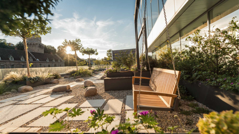 The castle on the Iron Road, © Dominik Stixenberger Garden with rocking bench, gravel path and plants, in the background a castle at sunset.