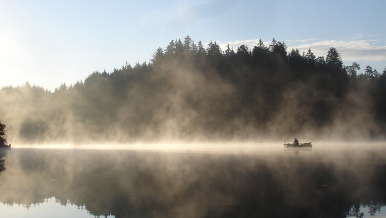 Gasthof Hanni KG, © Gasthof Hanni KG A boat on a misty lake in front of a wooded shore at sunrise.