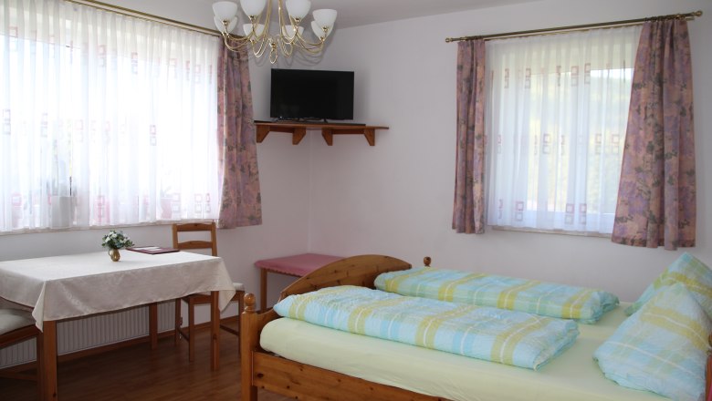 Multi-bed room, © Karl Buchner A bright room with a double bed, table, chairs and a TV on the wall.