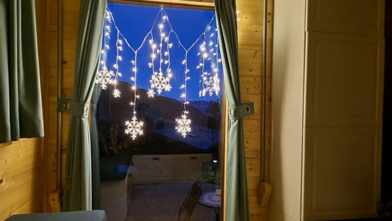 We also rent in winter!, © Villa to go Window with curtains and snowflake fairy lights, two candles on the windowsill.
