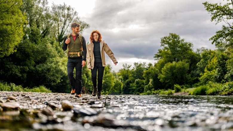 On the Leitha, © Wiener Alpen/Fülöp, Kremsl A woman and a man stroll happily along the gravel bed next to the Leitha, green forest in the background