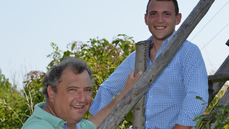 Waldschütz family, © Familie Waldschütz Two men smile into the camera, one sitting, the other standing on a wooden ladder outside.