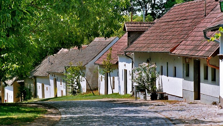 Wine cellar lane Pillichsdorf, © Thomas Falch A picturesque wine cellar lane with old, white wine cellars and cobblestones in Pillichsdorf, surrounded by green trees.