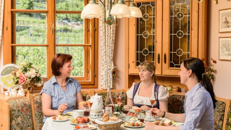 Breakfast room at Weinberghof Lagler, © Rita Newman Three women sit at a laid breakfast table in a cozy room with wooden furniture and large windows overlooking vineyards.