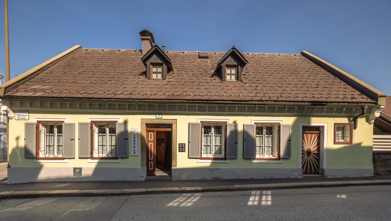 Leopold an der Ybbs, © © Niederösterreich Werbung/ Maximilian Pawlikowsky A traditional yellow house with a brown roof and green shutters on a street.