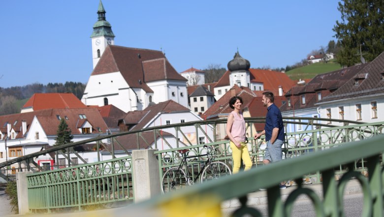 On a city tour through Scheibbs, © schwarz-koenig.at A couple stands on a bridge in Scheibbs with a church in the background.