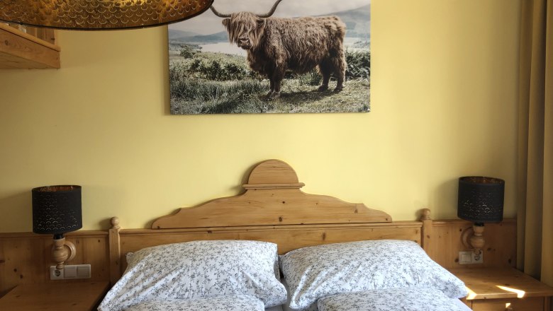 Room example for vacation at the Jauerling, © Romana Wiener Cozy bedroom with wooden furniture, double bed and picture of a highland cattle on the wall.