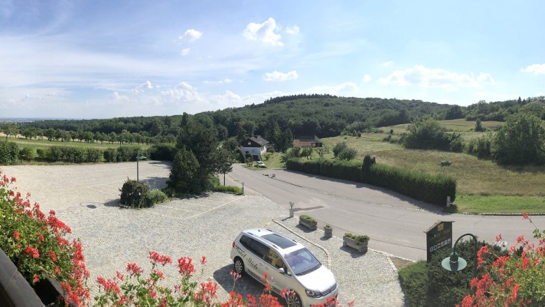 Foresight, © Hotel Stich Panoramic view of a rural landscape with hills and meadows from a hotel balcony.