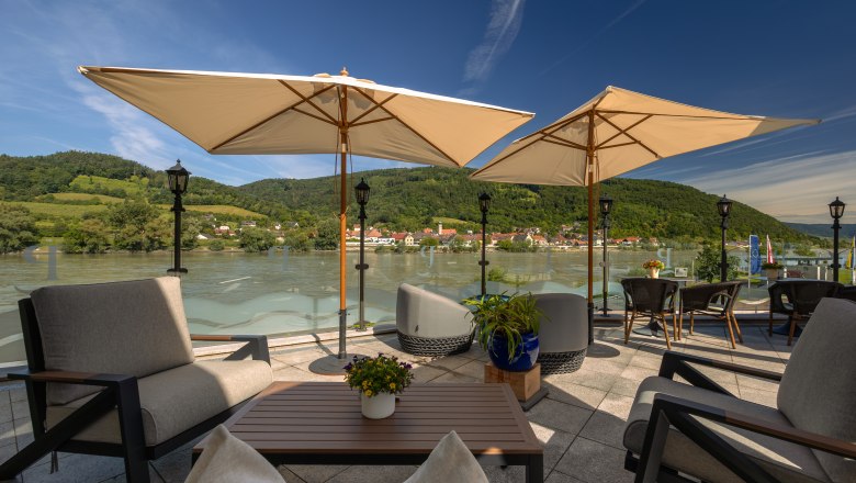 Hotel ResidenzWachau, © Niederösterreich Werbung / Maximilian Pawlikowsky Terrace with a view of the Danube and surrounding hills, equipped with parasols and seating furniture.