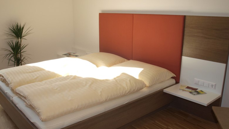 Guest room, © Wolfgang Rieder Modern guest room with double bed, red headboard and plants.