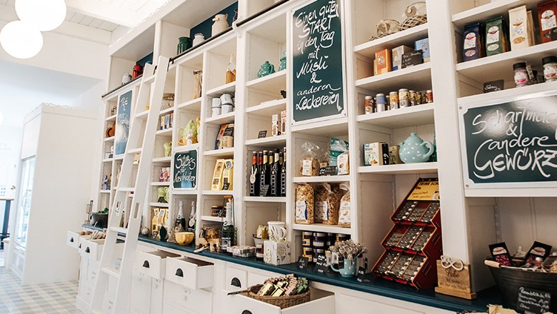 Eis-Greissler farm store inside, © Blochberger Eisproduktion GmbH Farm store with white wooden shelves and various products such as spices, chocolates and teas.
