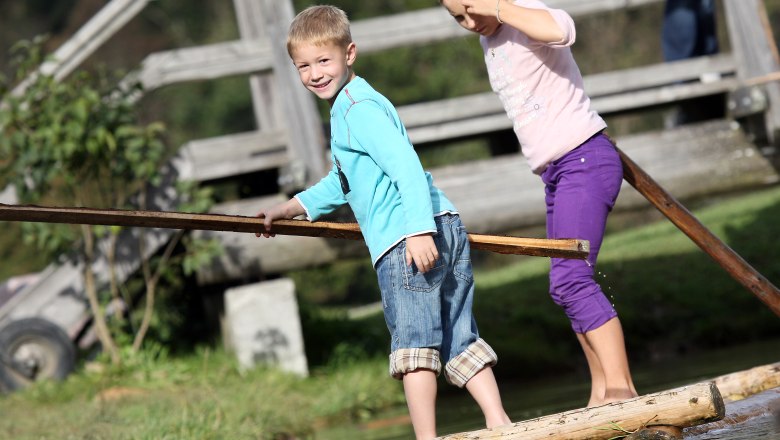 Gasthof Jagersberger, © weinfranz.at Two children balance on a wooden raft over water, in the background a wooden bridge.
