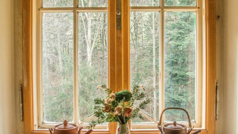 Orlet on the Rax, © Sofia Orlet Window with two teapots and a vase of flowers on the windowsill, forest in the background.