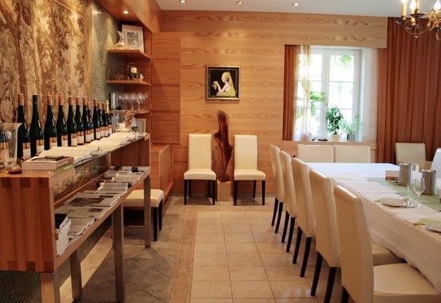 Tasting room, © Minkowitsch A tasting room with wooden walls, a long table with white chairs and bottles of wine on a shelf.