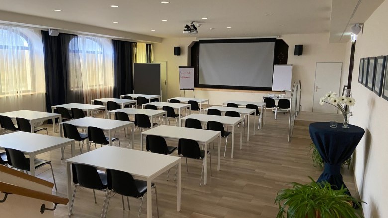 Seminar room, © Wiener Alpen An empty seminar room with white tables, black chairs and a large screen at the front.