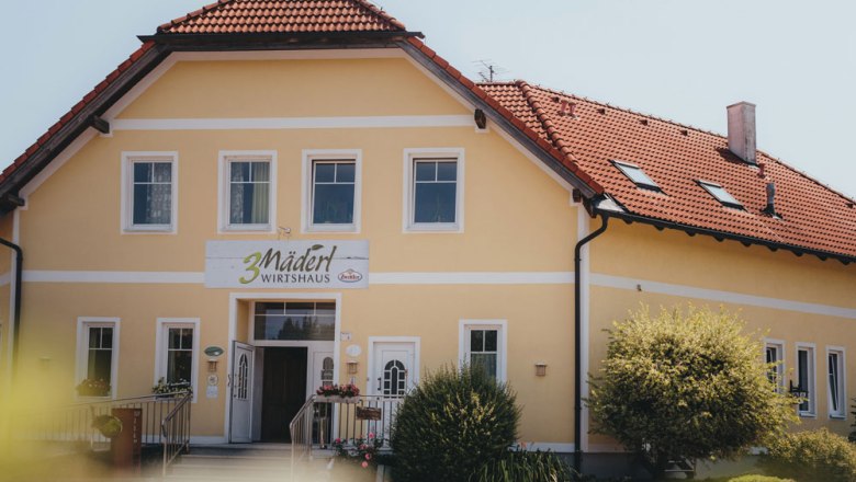 A typical Mostviertel inn, © Niederösterreich Werbung/Daniela Führer Yellow building with red roof and sign '3 Mädel Wirtshaus'.