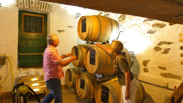 Veltsam production, © Familie Mayer Two people in a wine cellar with wooden barrels.