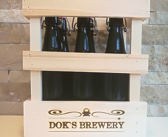 Beer selection, © Doks Brewery Wooden crate with three dark beer bottles from Dok's Brewery in front of a stone wall.