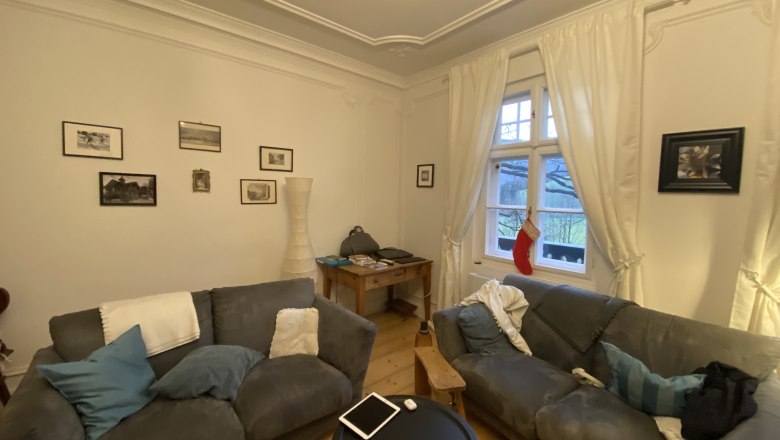 753e5cc4-a3ed-4959-8b93-e84a4e92cea7, © Martin Sturm Cozy living room with two grey sofas, a round table, pictures on the wall and a window with curtains and a Christmas stocking.