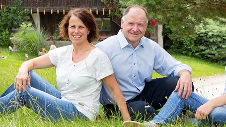 Christiane and Huber Eisinger, © Sinawehl Waltraud A man and a woman sit smiling on a lawn in front of a house.
