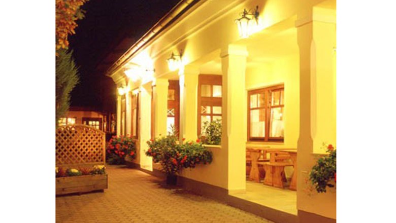 Wine tavern Gilg, © Weingut Gilg Illuminated entrance area of a traditional building with columns and flowers.