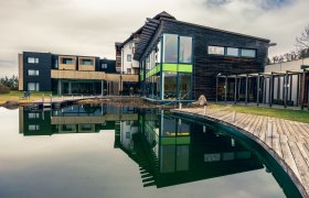 schwarzalm wellness, © Schwarz Alm Modern wellness hotel with wooden façade and large pond in the foreground.
