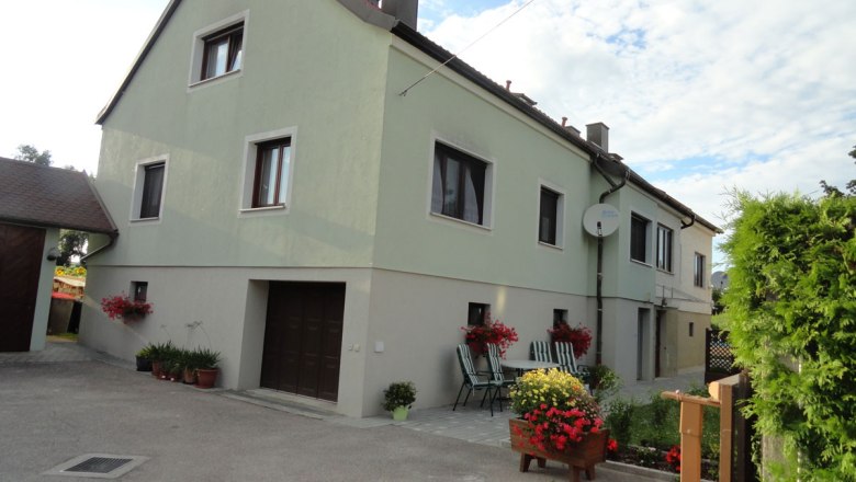 Exterior view of the house, © Schreiblehner Exterior view of a two-story house with green paint, flowers and garden furniture in the foreground.