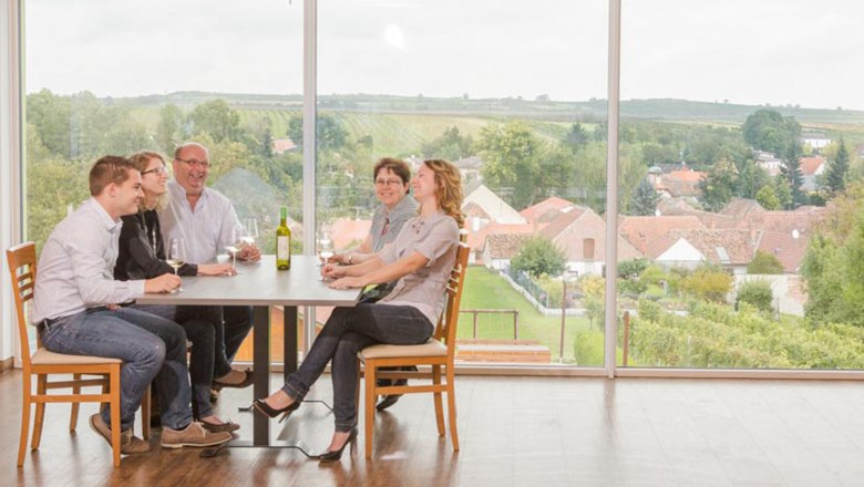 Dworzak family, © Astrid Bartl A family sits at a table with wine, with a landscape of houses and fields in the background.