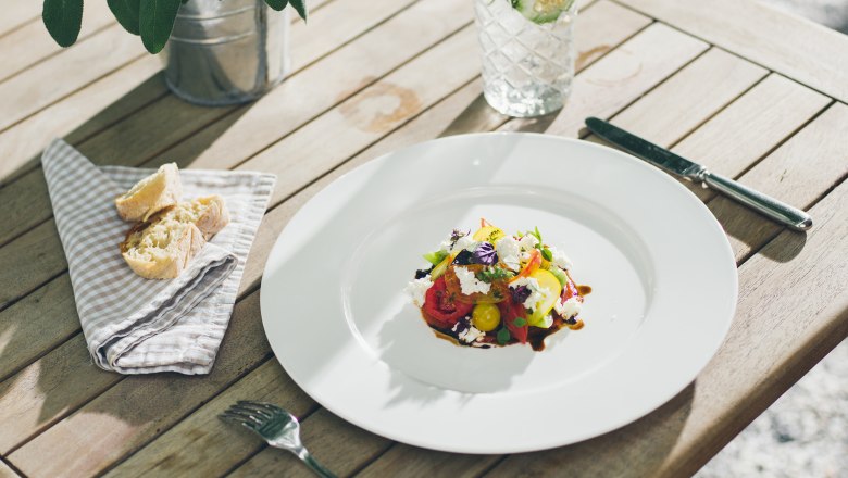 Culinary art at gourmet level, © Hofmeisterei Hirtzberger/Julius Hirtzberger An artfully arranged salad on a white plate, next to it a glass of water with cucumber slices and bread on a napkin.