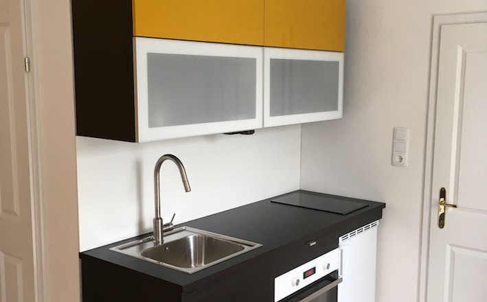 Greifenstein Old Post Office, © Eduard Renfer Small modern kitchen with yellow wall units, sink, hob and oven.