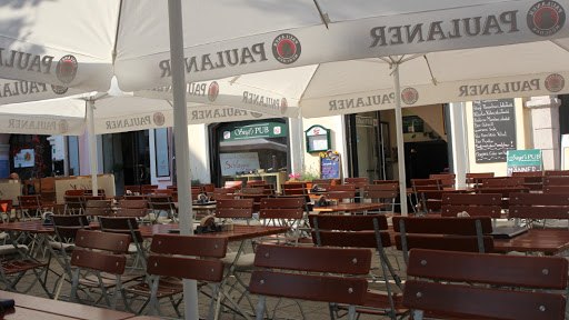 Siegl's Pub, © Siegl´s Pub - Simone Pichler Outdoor area of a pub with empty wooden benches and Paulaner parasols.
